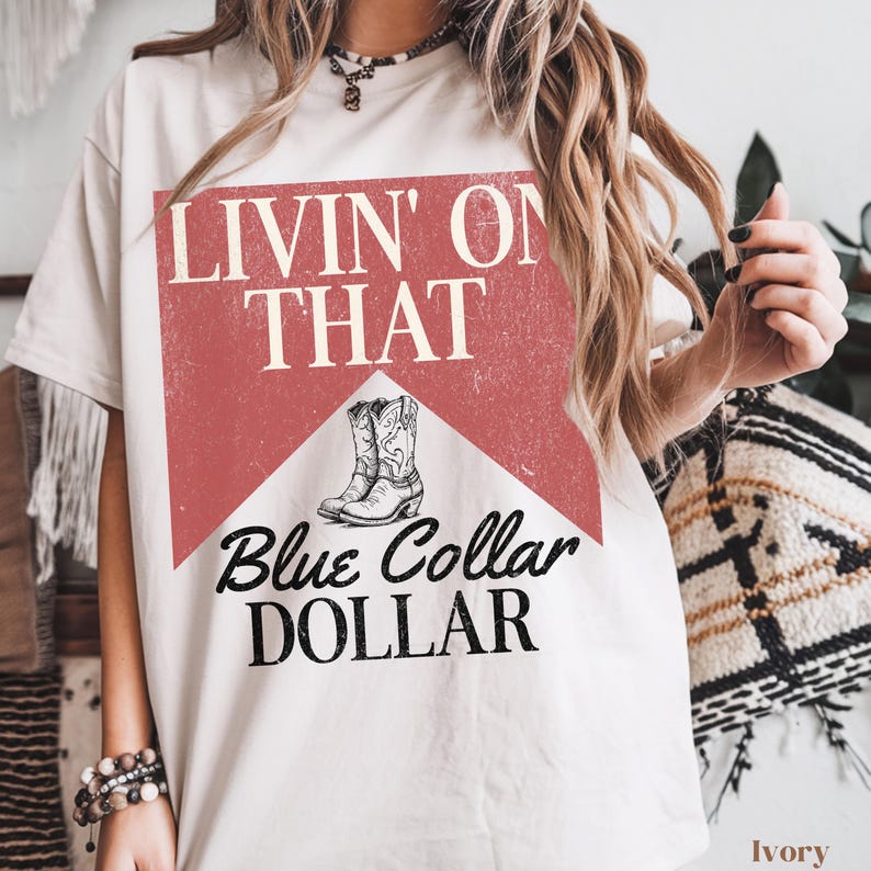 May include: White t-shirt with a red and white graphic that says "Livin' on That Blue Collar Dollar" with a pair of cowboy boots on the graphic.