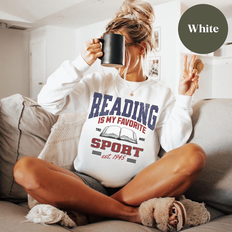 May include: White sweatshirt with a vintage-style graphic that says "Reading is my favorite sport est. 1945" with a book illustration.