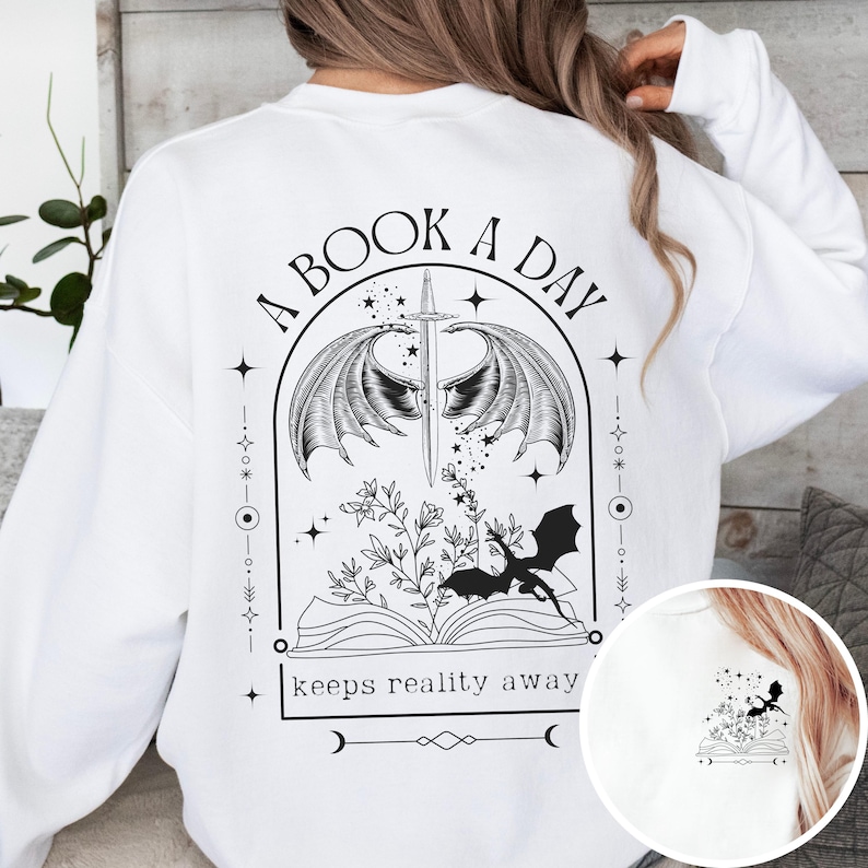 May include: White sweatshirt with a black graphic print of a book with wings, a sword, and a dragon. The text "A Book A Day Keeps Reality Away" is printed below the graphic.