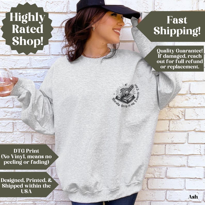 May include: Ash-colored sweatshirt with a crew neck. The graphic on the front features a book with a skeleton hand and the text "Morally Grey is my Favorite Color". The sweatshirt has long sleeves and is made of a soft material.