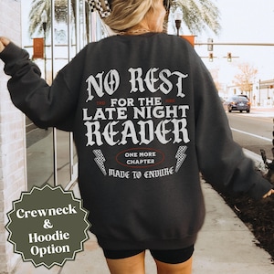 Peut inclure: Sweat-shirt gris fonc&eacute; avec l'inscription blanche "NO REST FOR THE LATE NIGHT READER". Le design comprend des &eacute;clairs et la phrase "ONE MORE CHAPTER MADE TO ENDURE". Une &eacute;tiquette verte indique les options col rond et sweat &agrave; capuche.