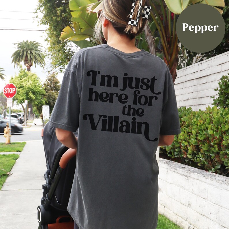 Puede incluir: Una camiseta gris oscuro con el texto "I'm just here for the Villain" impreso en la parte posterior en negro.