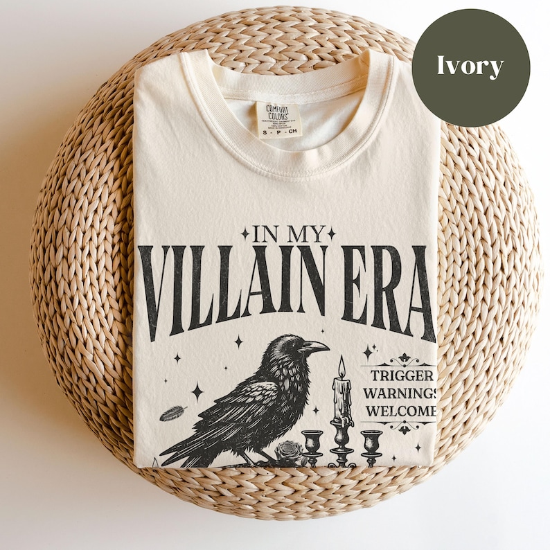 May include: A cream coloured t-shirt with a black raven illustration and the text "In My Villain Era" and "Trigger Warning: Welcome".
