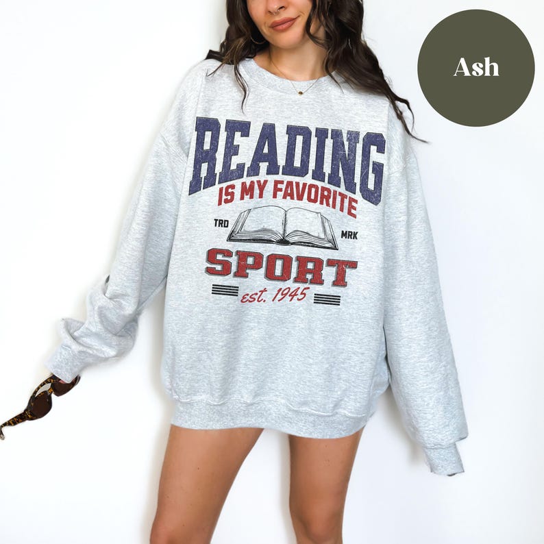 May include: A gray sweatshirt with the text "Reading is my favorite sport est. 1945" and an illustration of an open book. The text is in a vintage style font.