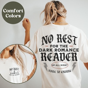 May include: White t-shirt with black text that reads "No Rest for the Dark Romance Reader" with a graphic of a book and lightning bolts. The text "Up All Night" and "Made to Endure" are also on the shirt.