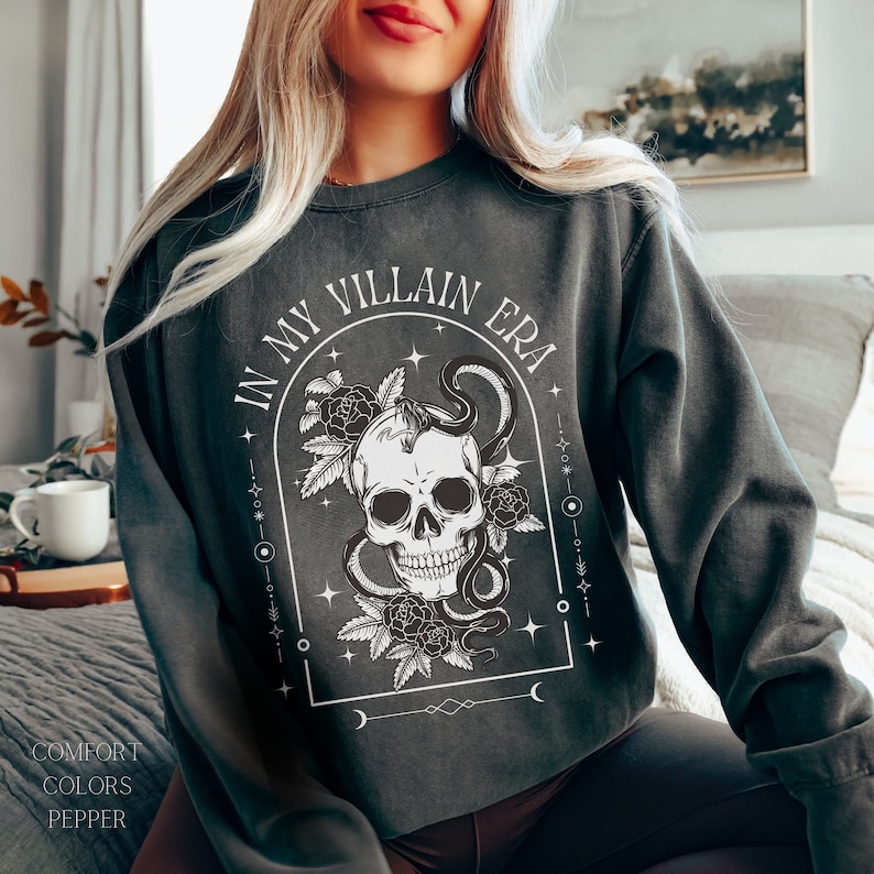 May include: A dark gray sweatshirt with a skull and snake graphic and the text "In My Villain Era".