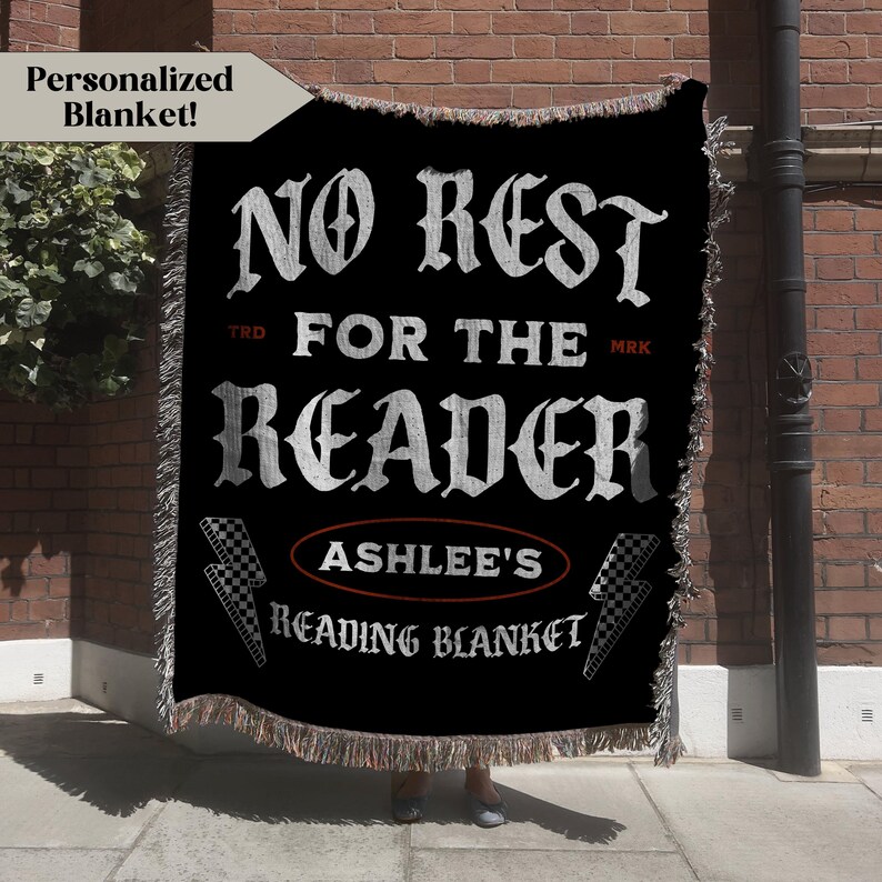 May include: Black woven blanket with white text that reads "NO REST FOR THE READER" and "ASHLEE'S READING BLANKET". The blanket has a fringed edge and a personalized design. A banner in the upper left corner says "Personalized Blanket!"