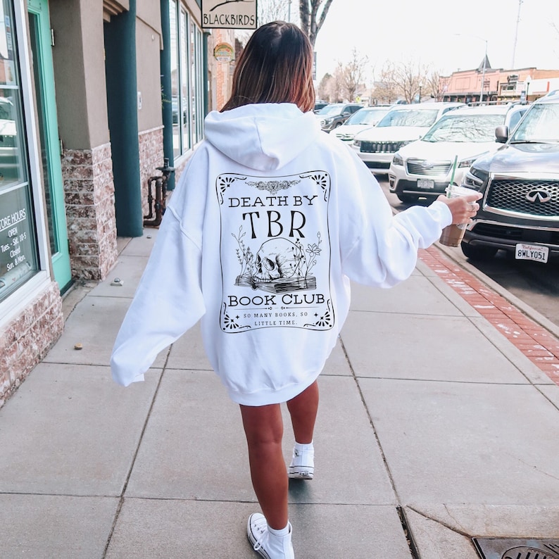 K&ouml;nnte beinhalten: Wei&szlig;er Kapuzenpullover mit einem schwarz-wei&szlig;en Grafikdruck auf der R&uuml;ckseite. Die Grafik zeigt einen Sch&auml;del, Blumen und den Text "Death by TBR Book Club. So many books, so little time."