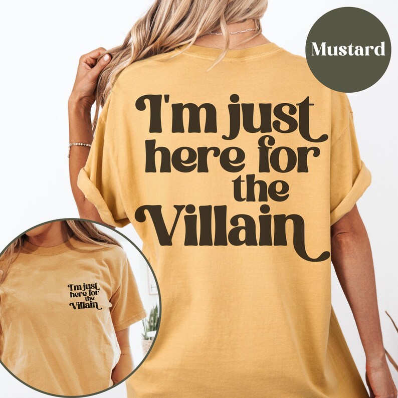 Puede incluir: Una camiseta amarilla mostaza con el texto "I'm just here for the Villain" impreso en negro. La camiseta tiene un corte holgado y cuello redondo.