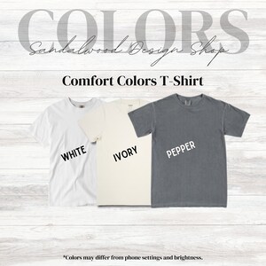 Puede incluir: Tres camisetas de diferentes colores: blanco, marfil y gris. Las camisetas est&aacute;n etiquetadas como "White", "Ivory" y "Pepper". El texto "Comfort Colors T-Shirt" est&aacute; en la parte superior de la imagen.