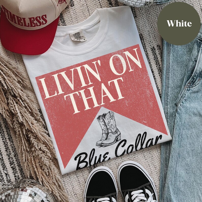 May include: White t-shirt with a red and white graphic that says "Livin' on That Blue Collar". The graphic features a pair of cowboy boots.