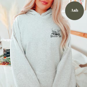 K&ouml;nnte beinhalten: Ein grauer Kapuzenpullover mit dem Text "Death by TBR" und einem Totenkopf-Motiv.