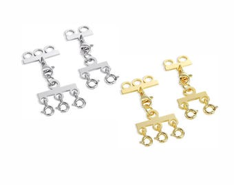 Può includere: Due set di chiusure per gioielli in argento e oro. Ogni chiusura ha tre piccoli anelli e una chiusura a moschettone. Le chiusure sono progettate per collegare più fili di collane o bracciali. Lo sfondo è bianco.