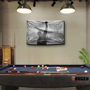 Puede incluir: Bandera en blanco y negro con la silueta de una persona con el puño en alto, con texto de Rocky Balboa. La bandera está colgada sobre una mesa de billar con bolas y tacos. La bandera tiene ojales dorados.