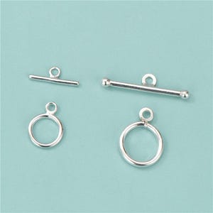 May include: Two sets of silver-toned toggle clasps for jewellery making. Each set consists of a circular ring component and a T-bar component, both featuring small loops for attachment. The metal has a smooth, reflective finish throughout.