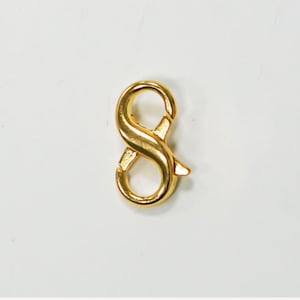 Puede incluir: Un cierre de mosquetón de metal en tono dorado con un diseño de doble extremo y dos aberturas con resorte. Este componente de joyería presenta un acabado liso y pulido con una forma curva en ocho para conectar piezas de joyería de forma segura.