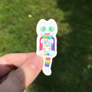 May include: A whimsical sticker featuring a white cat with green eyes and a clock face on its body. The cat has a colorful bow tie and a rainbow-striped tail. The clock shows the time as 3 o'clock.