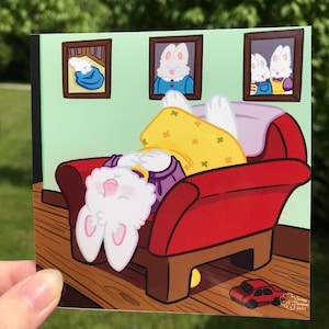 Op de afbeelding: Een vierkante sticker met een cartoonkonijn dat ontspant op een rode fauteuil. Het konijn draagt een gele jurk en een paars shirt. Drie ingelijste foto's van konijnen hangen aan de muur. Een rode speelgoedauto staat op de vloer. De sticker is gesigneerd "Scoopy Scribbles 2024."