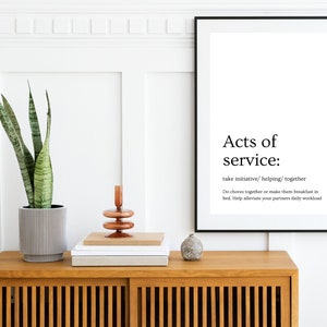 Könnte beinhalten: Ein schwarz-weiß gerahmter Druck mit dem Text "Acts of service: take initiative/helping/together Do chores together or make them breakfast in bed. Help alleviate your partners daily workload" auf weißem Hintergrund. Der Druck hängt an einer weißen Wand über einer Kommode aus Holz mit einer Topfpflanze und einem dekorativen Kerzenhalter.