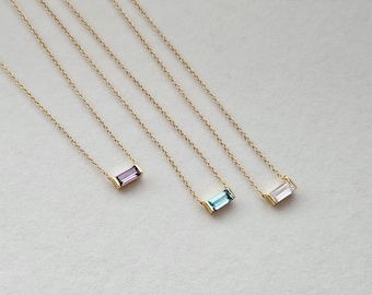 Könnte beinhalten: Drei goldene Halsketten mit verschiedenen Edelsteinen. Die Halsketten haben ein schlichtes Kettenmuster und einen rechteckigen Edelstein-Anhänger. Die Edelsteine sind lila, blau und klar.