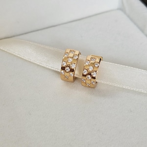 May include: A pair of gold hoop earrings with small clear cubic zirconia stones set in a geometric pattern.