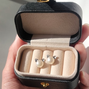 May include: A black velvet jewelry box with a white interior. The box is open and contains two pearl cat earrings.