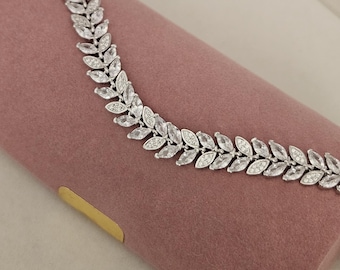 May include: A silver bracelet featuring a leaf design and clear cubic zirconia stones. The bracelet is displayed on a pink velvet background.