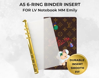 May include: A5 6-ring binder insert for LV Notebook MM Emily. The item features a gold-colored metal 6-ring mechanism attached to a clear plastic sheet, positioned next to a brown notebook cover with a repeating logo pattern and stickers.