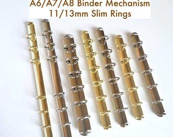 May include: Seven metal binder mechanisms with slim rings in gold and silver finishes, arranged vertically. The text A6/A7/A8 Binder Mechanism 11/13mm Slim Rings is displayed above the items. Each mechanism features multiple circular rings attached to a central spine.