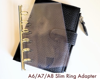 May include: A clear plastic ring adapter with a gold-colored metal spine featuring six rings, placed over a black textured wallet. The text A6/A7/A8 Slim Ring Adapter Fits TN, Wallet, Passport Cover is printed in dark red at the bottom of the image.