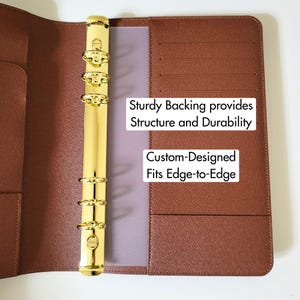 May include: A brown textured planner binder featuring a gold-colored six-ring metal mechanism. The interior includes card slots and pockets. Text on the binder reads: Sturdy Backing provides Structure and Durability, Custom-Designed Fits Edge-to-Edge.