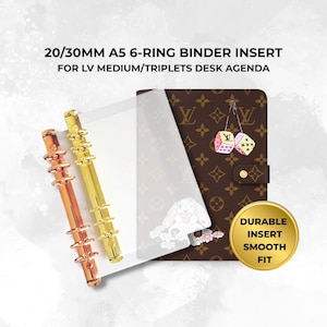 May include: A 20/30mm A5 6-ring binder insert for LV medium/triplets desk agenda. Includes two metallic ring mechanisms in rose gold and gold, a clear plastic sheet, and a brown monogram agenda cover with dice and rabbit graphics. Text reads: DURABLE INSERT SMOOTH FIT.