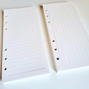 May include: Two white rectangular paper inserts for a planner, each featuring six punched holes along the left side. The left insert has horizontal lines, while the right insert has vertical lines, both designed for organized note-taking and planning.