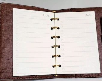 May include: A brown leather-textured planner with a six-ring gold-tone metal binder mechanism. The open planner features white pages with horizontal lines, checkboxes, and the word "ToDo" printed at the top of each page.