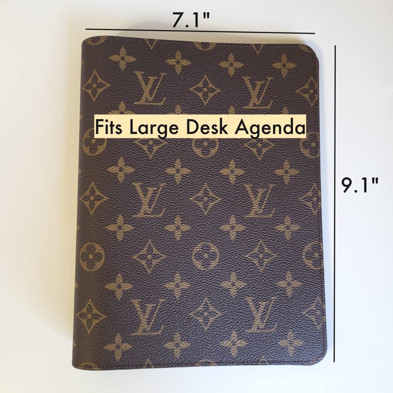 May include: A brown and tan monogram patterned agenda cover featuring the text Fits Large Desk Agenda. The cover measures 7.1 inches in width and 9.1 inches in height, displaying a repeating logo design across the entire front surface.