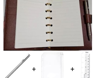 May include: A brown leather bound planner with gold rings and a white lined paper insert. The planner is open to show the lined paper. A silver pen, a clear plastic page protector, and a ruler with the word "TODAY" printed on it are included.