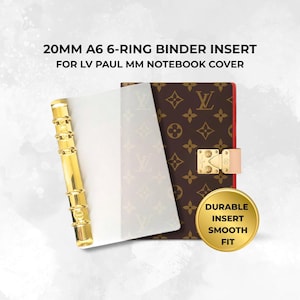 May include: A 20mm A6 6-ring binder insert for LV Paul MM notebook cover. The insert features a gold-toned metal ring mechanism and a clear plastic sheet. Beside it is a brown notebook cover with a repeating monogram pattern and a gold-tone clasp.