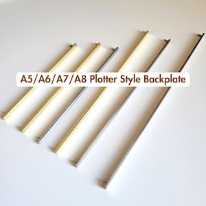 May include: A collection of six A5/A6/A7/A8 Plotter Style Backplate metal bars arranged diagonally. The bars feature varying metallic finishes including gold, silver, and dark gunmetal tones, each with small mounting pins at the ends.
