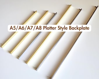 May include: A collection of six A5/A6/A7/A8 Plotter Style Backplate metal bars arranged diagonally. The bars feature varying metallic finishes including gold, silver, and dark gunmetal tones, each with small mounting pins at the ends.