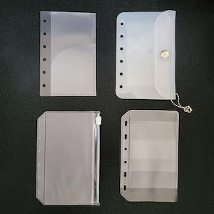 May include: Four clear plastic zippered pouches with different designs. The pouches have holes for a binder and are designed to hold papers or other small items.