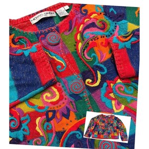 May include: A vibrant, patchwork-style cardigan with a riot of colors including red, blue, green, and orange. The sweater features intricate embroidered details and spiral button closures. The label reads "MICHAEL SIMON".