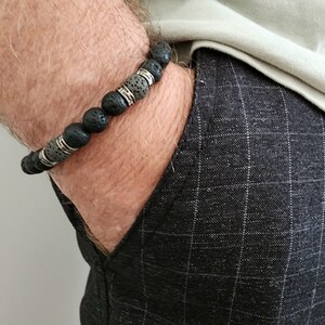 May include: A black and grey beaded bracelet with silver accents. The bracelet is made of lava rock and metal beads.
