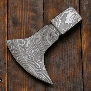 May include: A hand-forged axe with a Damascus steel blade and a wooden handle. The blade has a distinctive wavy pattern.