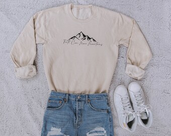 May include: A beige long-sleeved sweatshirt with a black mountain graphic and the text "Faith Can Move Mountains".