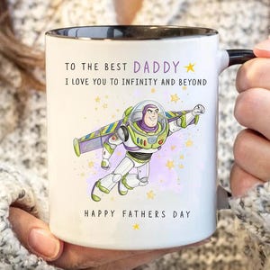 Puede incluir: Taza de cer&aacute;mica blanca con interior y asa negros. La taza presenta una colorida ilustraci&oacute;n de Buzz Lightyear y el texto "TO THE BEST DADDY, I LOVE YOU TO INFINITY AND BEYOND, HAPPY FATHERS DAY."