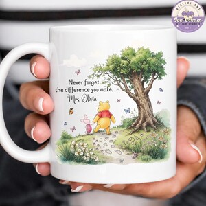 May include: White ceramic mug featuring a colorful illustration of Winnie the Pooh and Piglet walking on a path. The mug has the text "Never forget the difference you make. Mrs. Olivia."