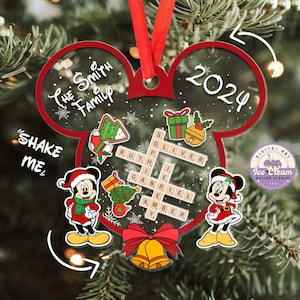 May include: A red and white Christmas ornament shaped like Mickey Mouse's head. The ornament is decorated with a snowflake pattern, a Christmas tree, a gingerbread man, and a bell. The ornament also features a crossword puzzle with the names "Oliver", "Ruth", "Gabriel", "Je", and "Amber". The ornament says "The Smith Family" and "2024" on it.