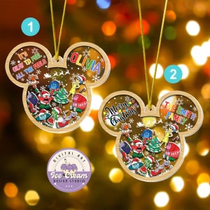 May include: Two wooden Christmas ornaments shaped like Mickey Mouse ears. The ornaments are clear and show a scene from the movie Inside Out. The first ornament has the text "It's okay to feel all the feels" and "Olivia". The second ornament has the text "Merry Christmas" and "The Smith Family".