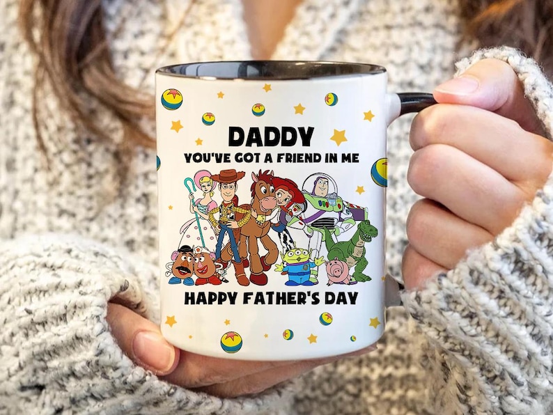 Puede incluir: Taza de cer&aacute;mica blanca con interior y asa negros, con un gr&aacute;fico colorido de personajes de dibujos animados y el texto "DADDY YOU'VE GOT A FRIEND IN ME HAPPY FATHER'S DAY". La taza est&aacute; decorada con estrellas y gr&aacute;ficos de bolas amarillas.