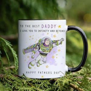 Puede incluir: Taza de cer&aacute;mica blanca con asa y borde negros, con una imagen de dibujos animados de Buzz Lightyear y el texto "TO THE BEST DADDY, I LOVE YOU TO INFINITY AND BEYOND, HAPPY FATHERS DAY". La taza est&aacute; decorada con estrellas.